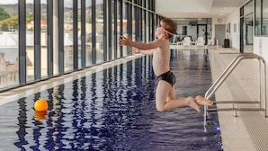 Un niño saltando a una piscina con una pelota de baloncesto en el aire.