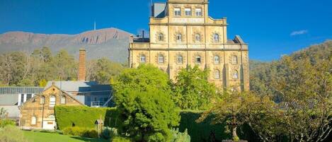 A large, historic building with a prominent clock tower, surrounded by lush greenery and a mountainous backdrop.
