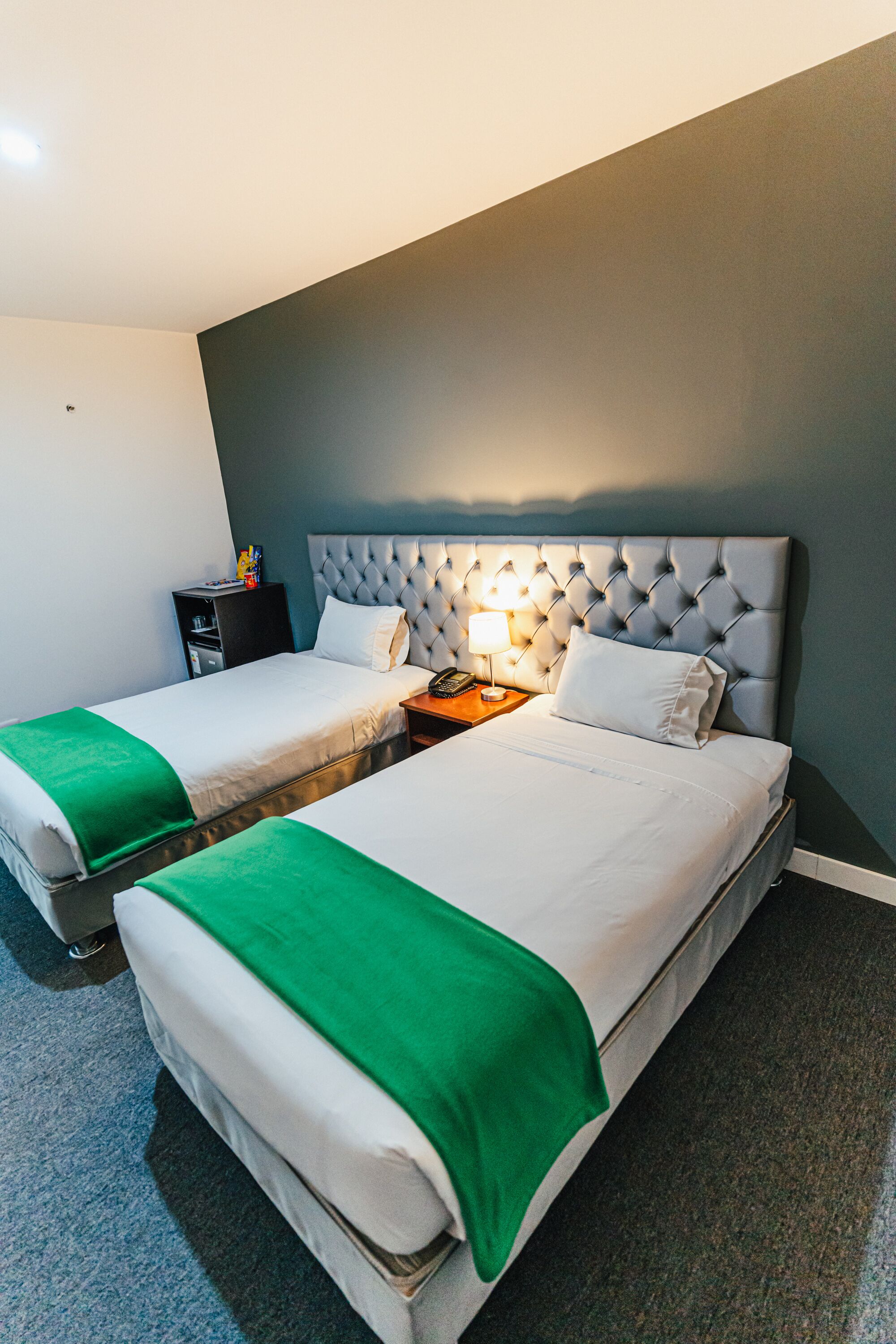A hotel room with two beds, a nightstand, and a lamp.