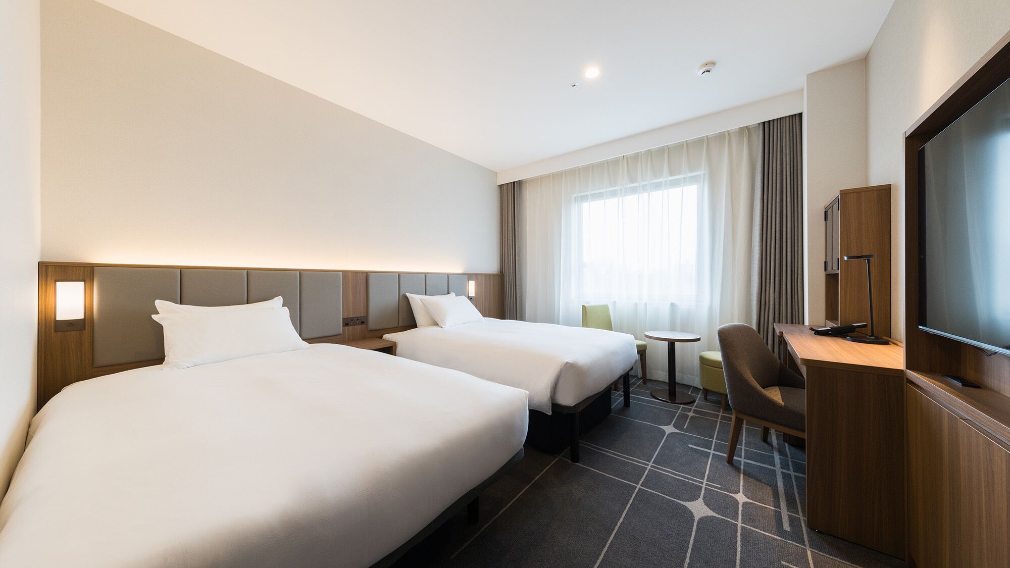 Hotelkamer met twee bedden, een bureau, een stoel, een televisie en een raam met gordijnen.