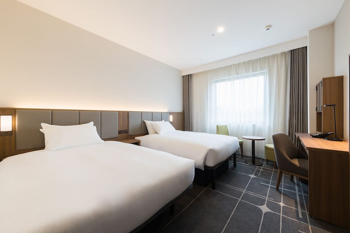 A hotel room with two beds, a desk, a chair, a television, and a window with curtains.
