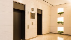 A modern elevator area with two elevators, a directory sign, and a wall-mounted planter with greenery. - JR-East Hotel Mets Mejiro (Tokyo)