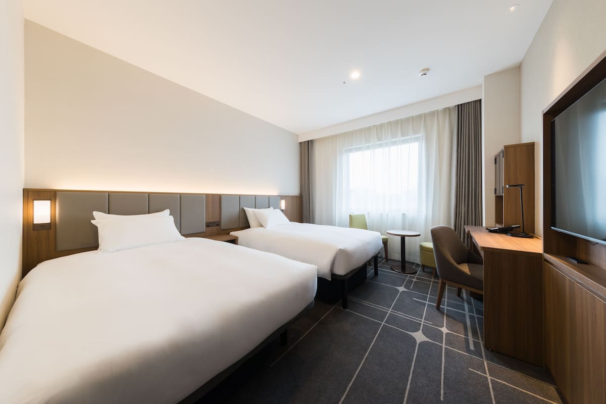 A hotel room with two beds, a desk, a chair, a television, and a small table.