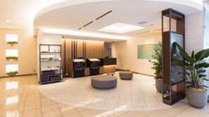 A modern lobby with a curved ceiling, a reception desk, a self-service kiosk, and a seating area with ottomans. - JR-East Hotel Mets Mejiro (Tokyo)