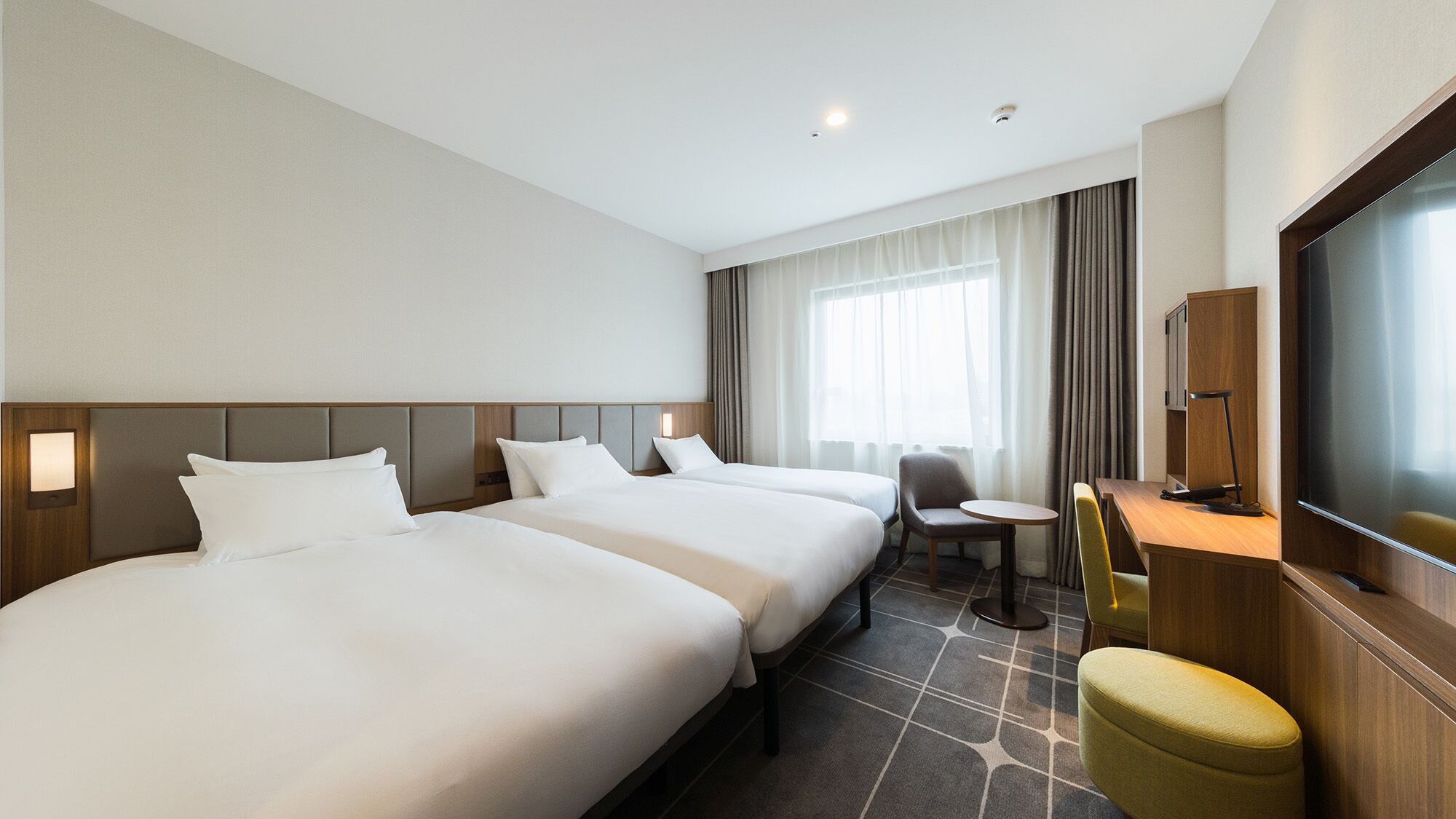 Een hotelkamer met twee bedden, een bureau, een stoel, een televisie en een raam met gordijnen.
