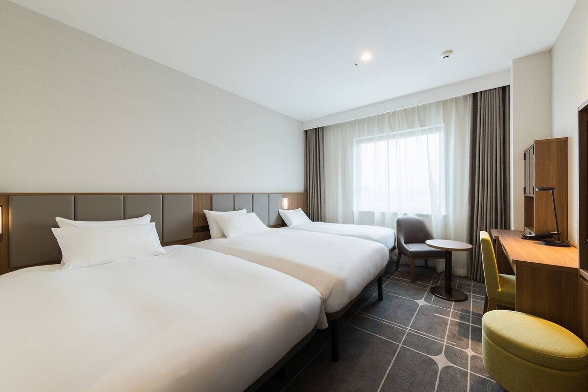 A hotel room with two beds, a desk, a chair, a television, and a window with curtains.