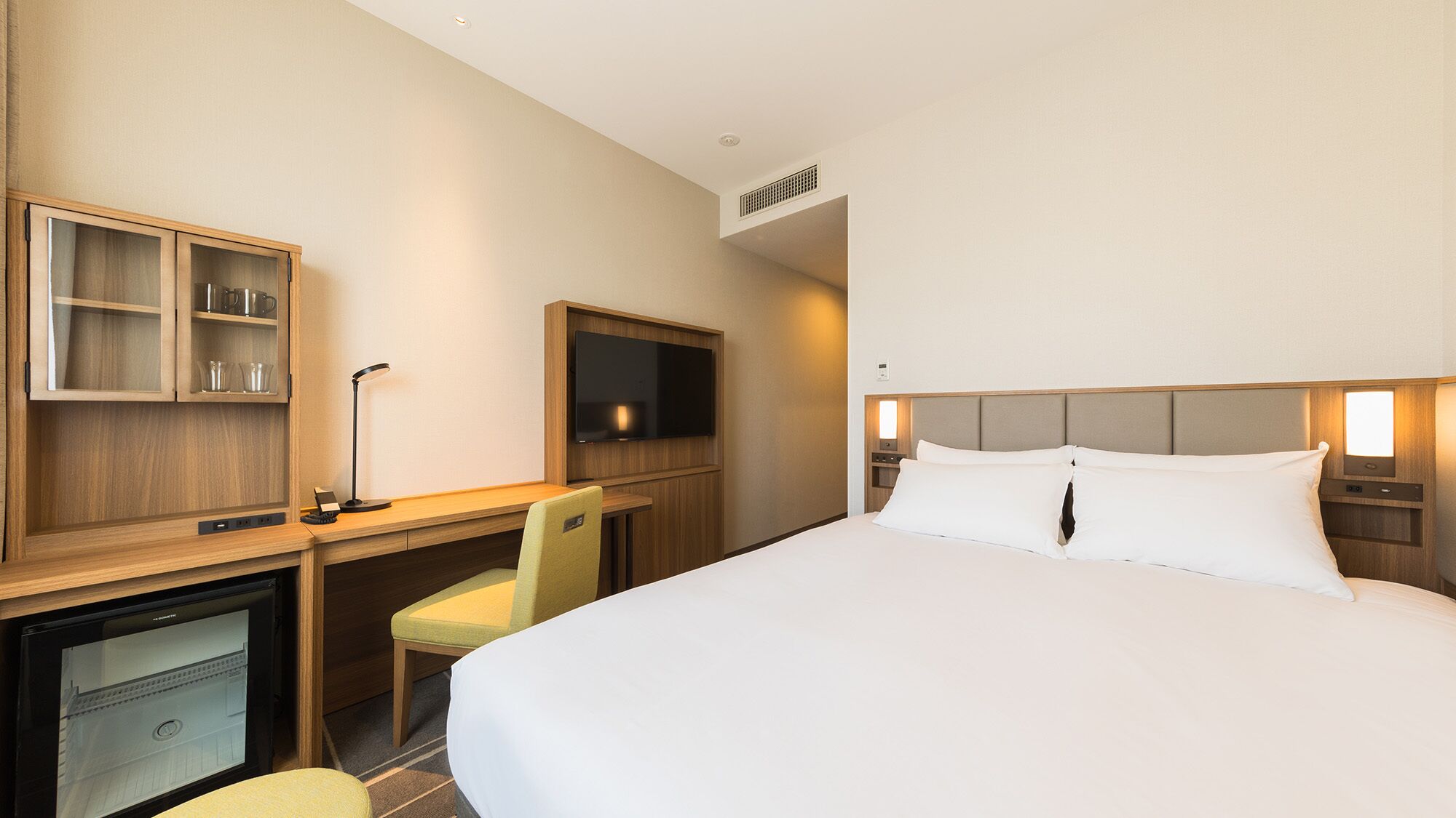 Een hotelkamer met een bed, bureau, stoel, televisie en een minibar.
