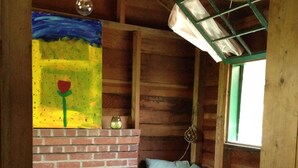 Interior acogedor de una cabaña con chimenea de ladrillo, un banco con cojines y un cuadro sobre la chimenea.