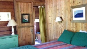 Una habitación de madera con una cama, una mesita de noche y un cuadro en la pared.