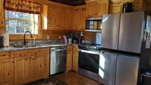 A kitchen with wooden cabinets, stainless steel appliances, a dishwasher, and a window with a view of trees.