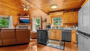 A spacious living area with a leather sofa, a black cabinet, and a kitchen with wooden cabinets and stainless steel appliances. - Beautiful Open Views, Very Private, Deck Gas Fireplace on all year & more! (Gatlinburg)