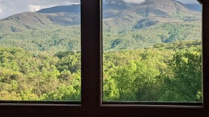 A view through a window of a mountainous landscape with dense green forests and a mountain peak in the distance.