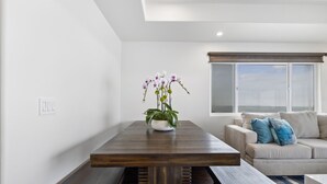A modern living room with a wooden dining table, a sofa with blue cushions, and a potted orchid plant.