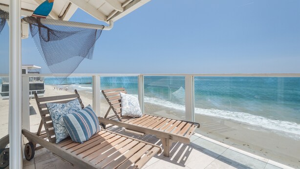 A wooden deck with a hammock, two lounge chairs, and a view of the ocean.