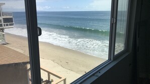A view of the ocean through a window, with a sandy beach visible.