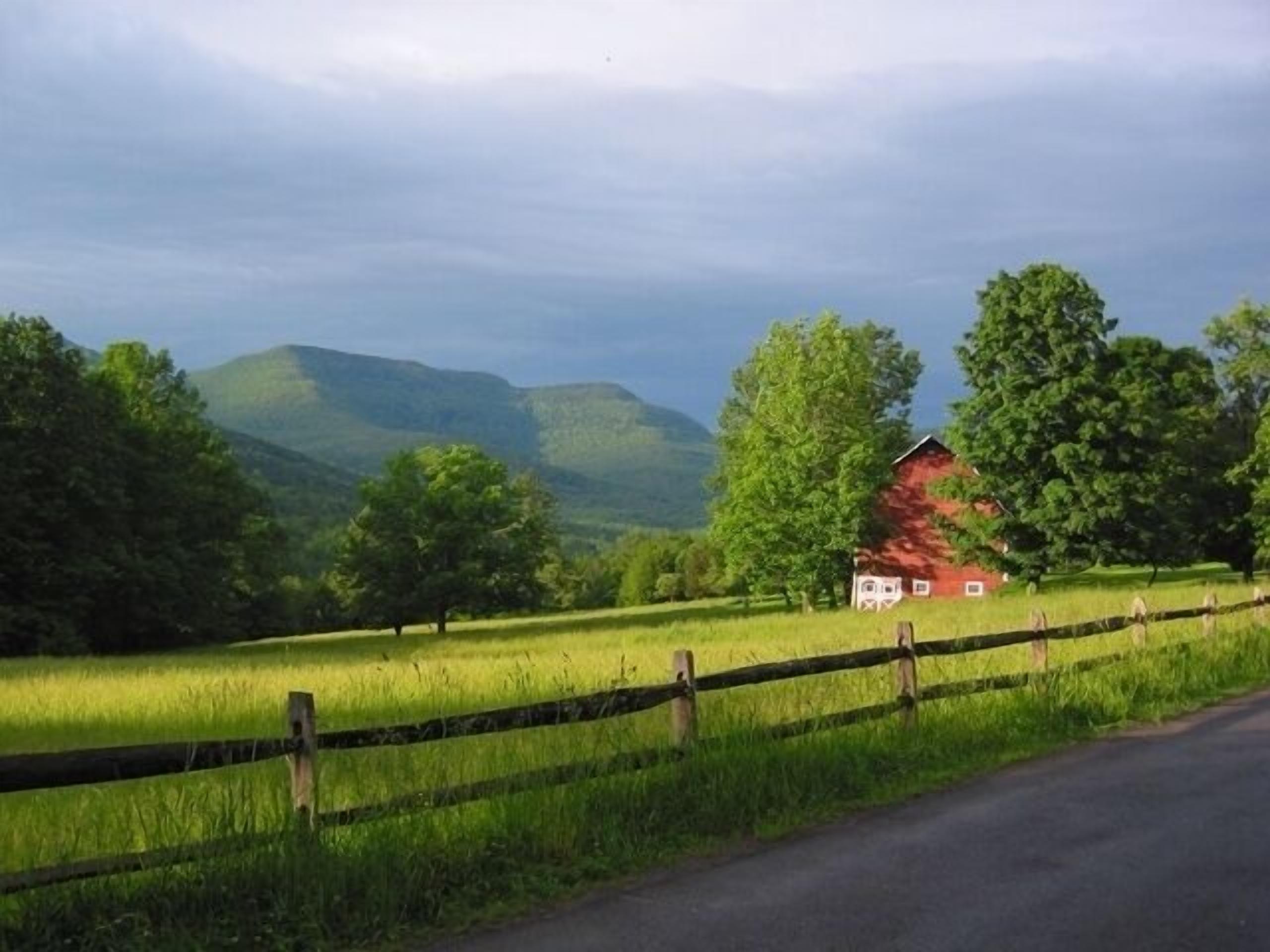 A rural landscape with a red barn, green fields, and a wooden fence.