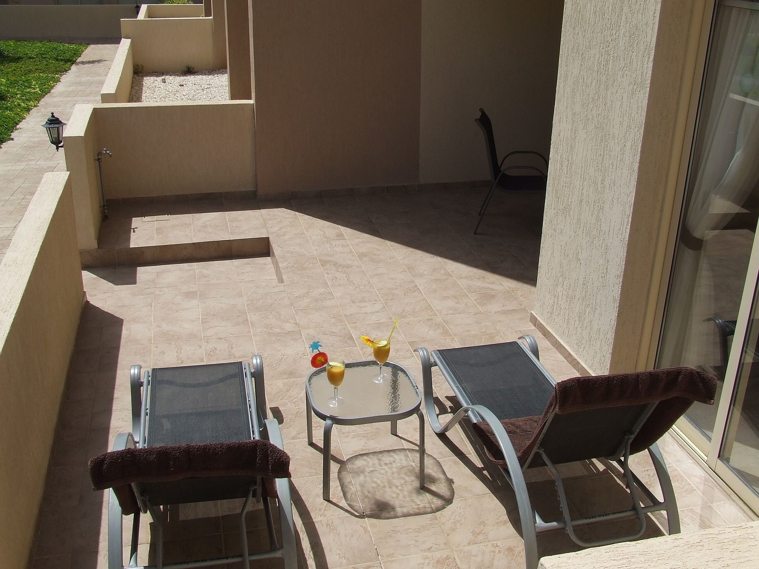 Een zonnig buitenterrein met twee tafels en stoelen van metaal, een kleine ronde tafel met een glazen blad, en een decoratief object op de tafel.