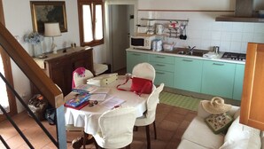A dining area with a table set for two, a kitchen with green cabinets, and a staircase leading to another room. - Magnolia, charming residence in the Barchessa of Venetian Villa: Villa Pastori (Mira)