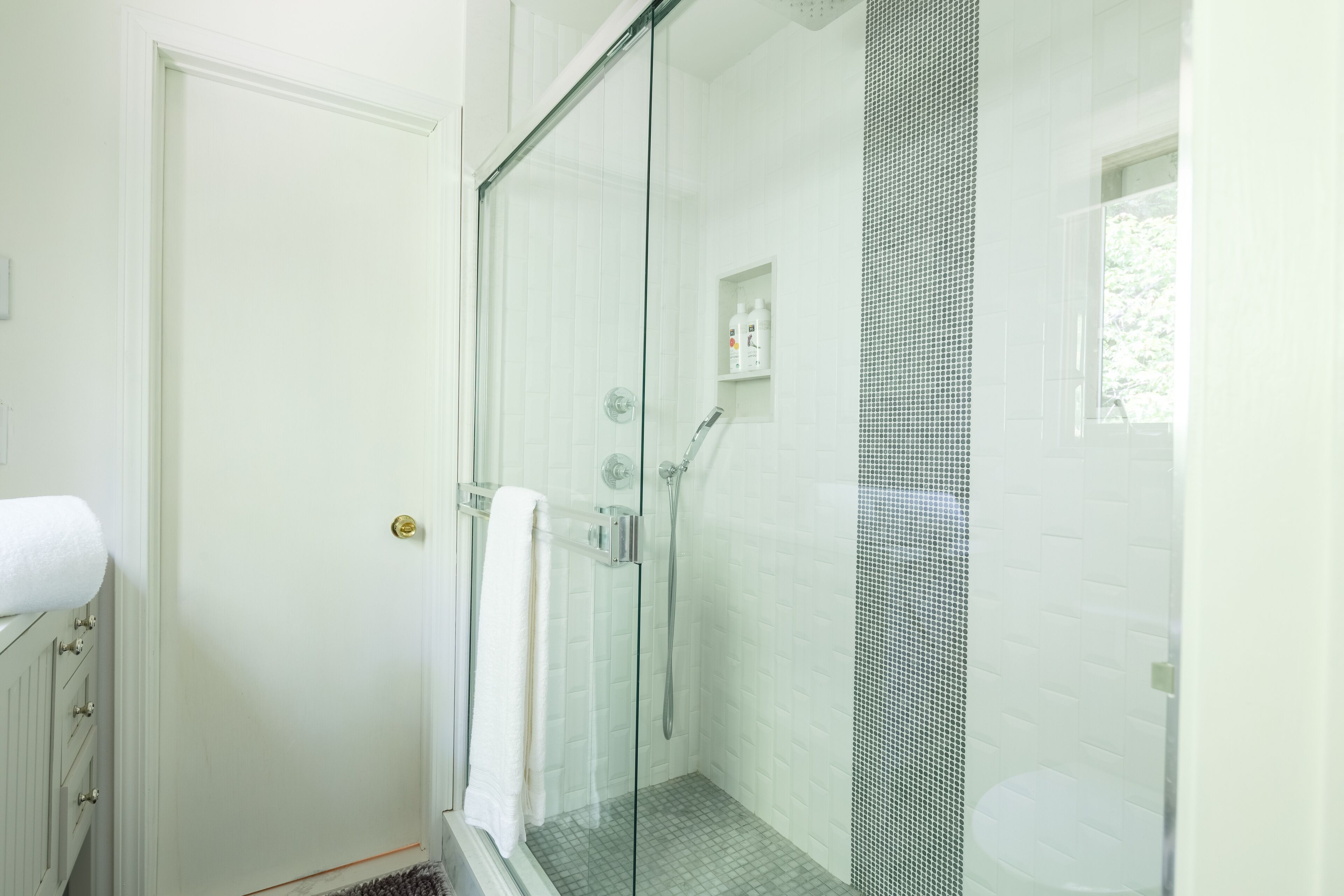 Une salle de bain moderne avec une douche à parois de verre, un mur recouvert de carreaux blancs et une petite étagère contenant des articles de toilette.