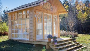 Una baita di legno con ampie finestre, un portico con gradini e piante in vaso.