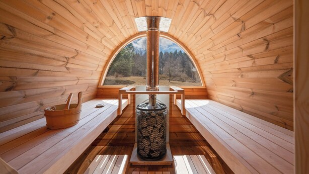 Ambiente in legno con camino centrale, panche e una finestra vista foresta.