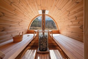 Un interior de madera con una chimenea central, bancos y un ventanal con vistas al bosque.