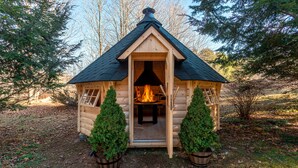 Un piccolo chalet in legno con camino, circondato da alberi e piante in vaso.