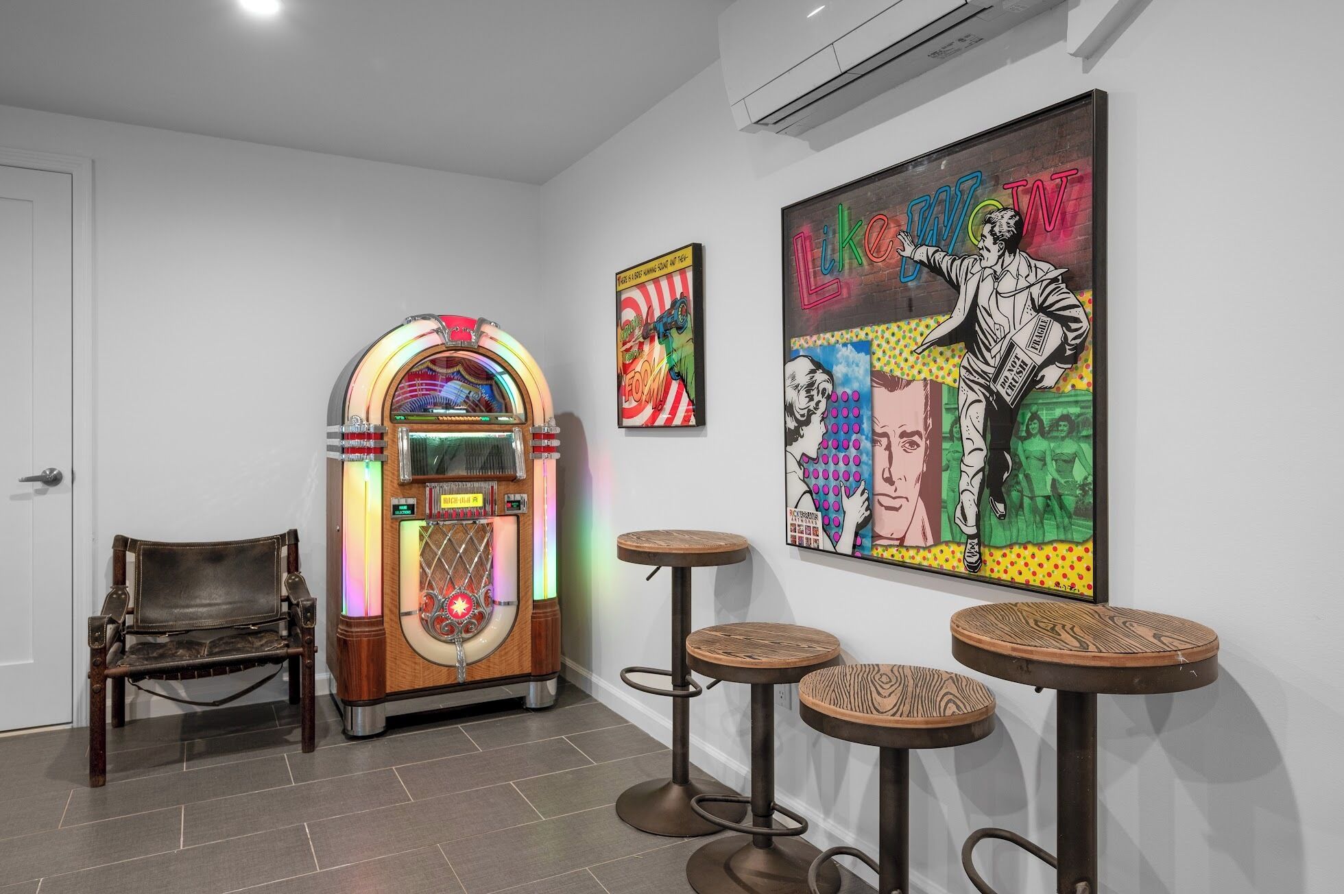Ein Raum mit Jukebox, Barhocker und Bildern an der Wand.