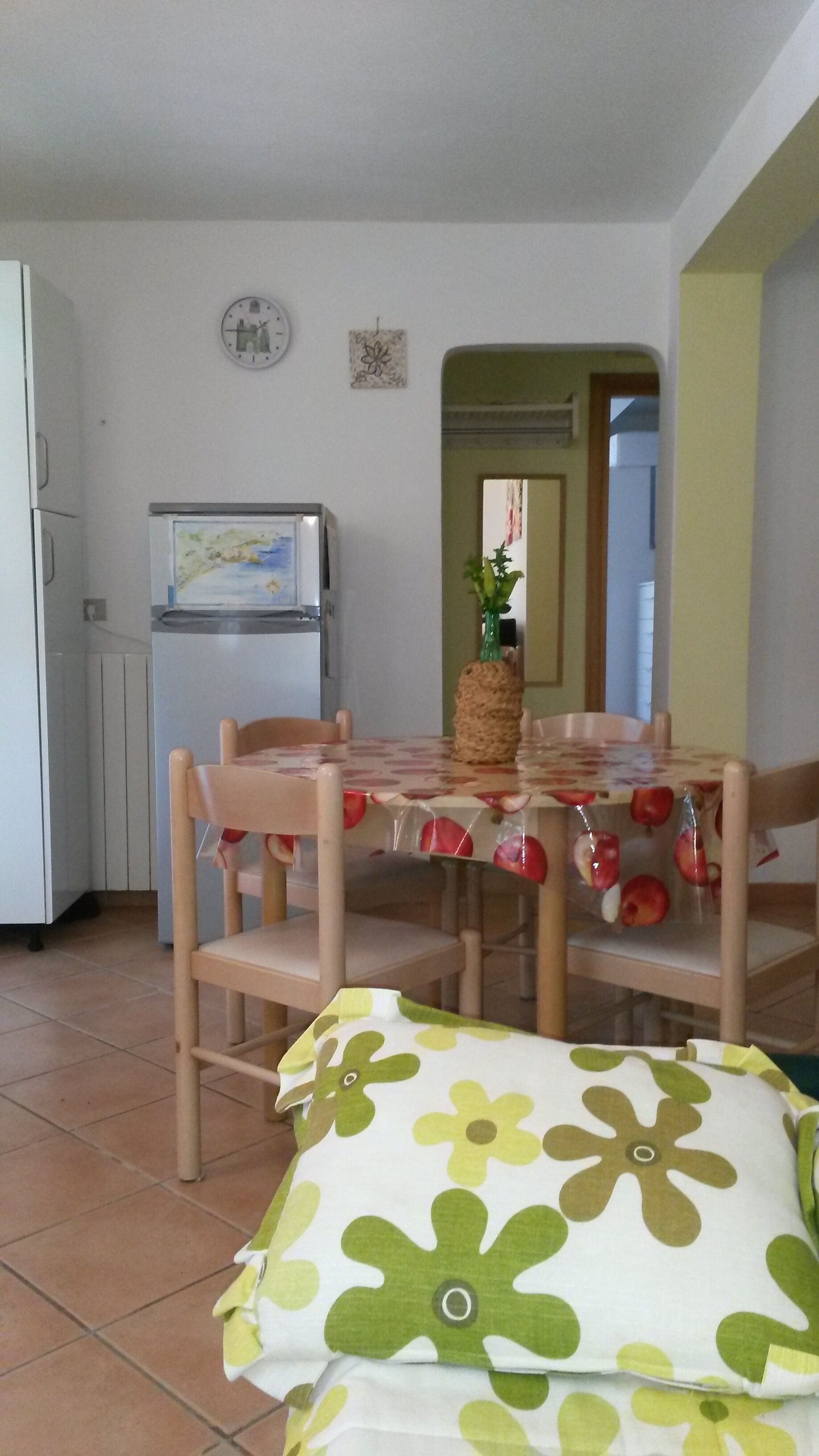 Een eetruimte met een tafel voor vier personen, een witte koelkast, een klok en een klein decoratief item aan de muur.