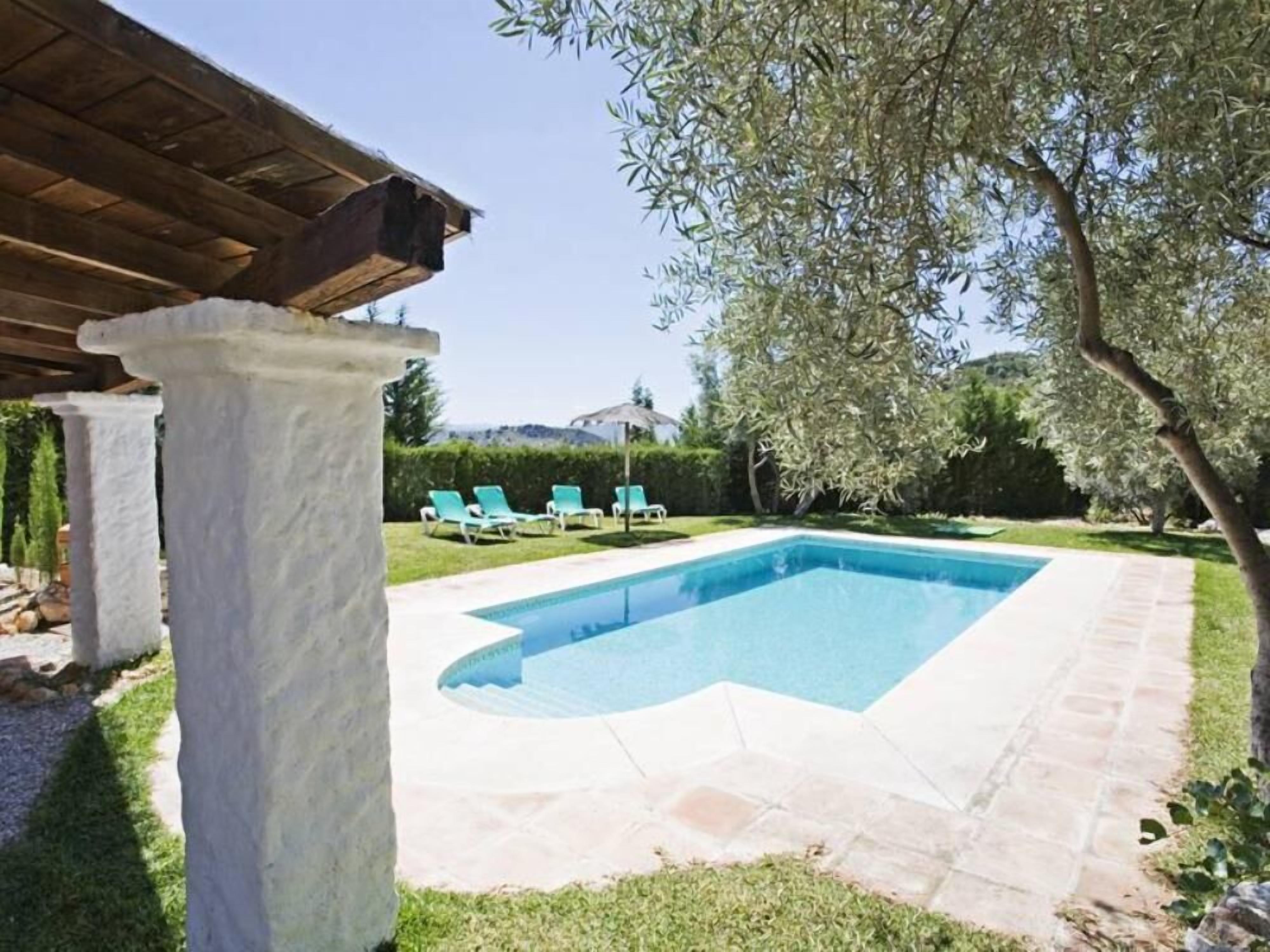 A swimming pool with a stone deck, surrounded by a grassy area and a pergola structure.