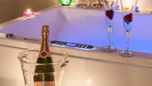 Eine Champagnerflasche in einem Glas-Eisbecher, zwei Champagnergläser mit Erdbeeren und eine Wanne mit Kerzen.