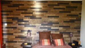 A bedroom with a herringbone-patterned wooden wall, a bed with two pillows, two bedside tables with lamps, and a small decorative plant. - Bed and Breakfast in the hinterland of Monaco (Peille)