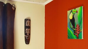 A room with a wooden headboard, a wall-mounted artwork of a toucan, and a vase with flowers. - Bed and Breakfast in the hinterland of Monaco (Peille)