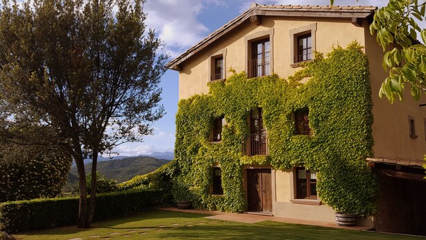 Un bâtiment aux murs recouverts de lierre, avec une pelouse bien entretenue et une vue sur des collines lointaines.