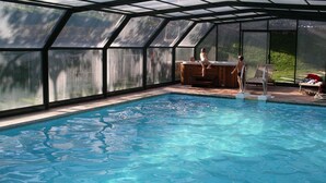 Une piscine dotée d’une structure en verre, d’une terrasse en bois et d’un jacuzzi.