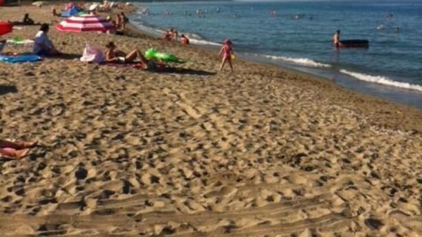 Een zandstrand met parasols en mensen.