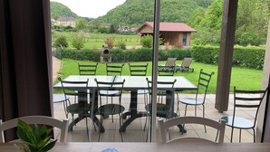 A dining area with a table and chairs, a view of a green landscape with houses, and a stone oven.