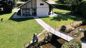 A white building with a sloped roof, a covered patio, and a small bridge over a stream.