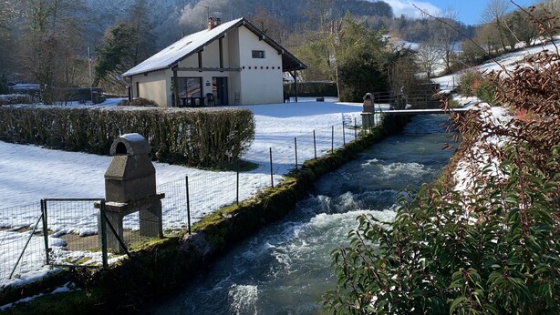 A building with a snow-covered roof, a small outdoor seating area, and a view of a river.