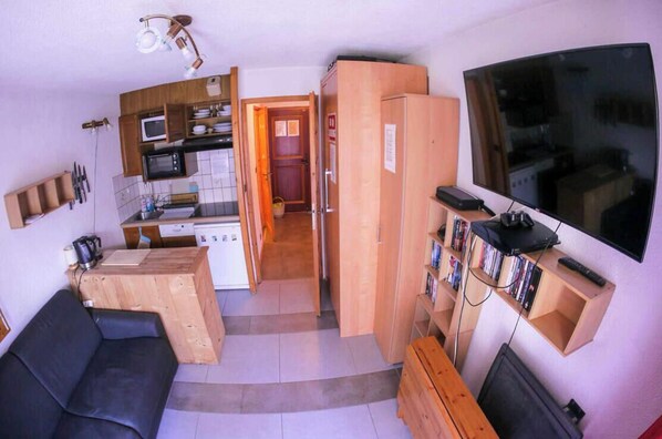 Ein gemütlicher Wohnraum mit einer Küchenzeile, einem Flachbildfernseher, einer Couch und einem Holzschrank.