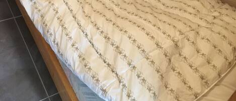 A small, single-bed room with a wooden frame, a white mattress with floral patterns, and a small shelf above the bed.