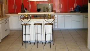 Una cocina con gabinetes rojos, encimeras blancas y tres taburetes negros.