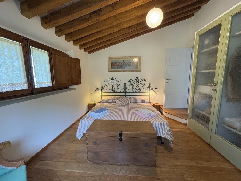 Un dormitorio con techo de madera, una cama con ropa de cama a rayas, un aparador y una puerta con paneles de vidrio esmerilado.