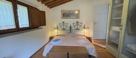 Un dormitorio con techo de madera, una cama con ropa de cama a rayas, un aparador y una puerta con paneles de vidrio esmerilado.