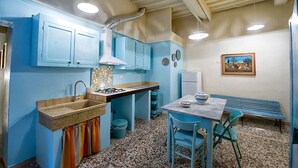 A compact kitchen with blue cabinets, a gas stove, and a dining area with a bench and chairs.