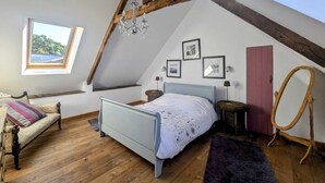 Un dormitorio con techo inclinado, una cama, un ventanal y una silla de madera.