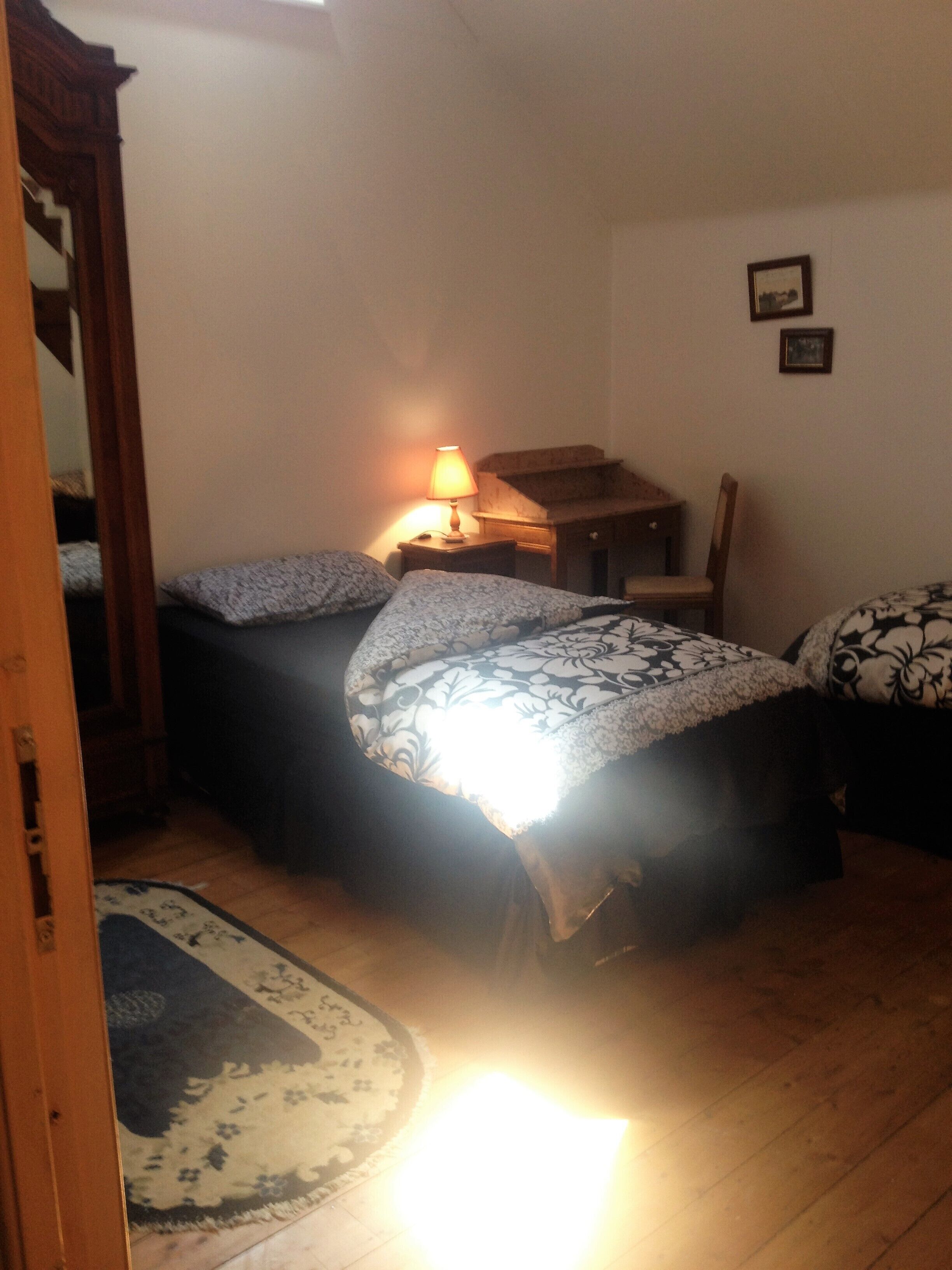 Une petite pièce faiblement éclairée, avec deux lits, un bureau en bois et une chaise.