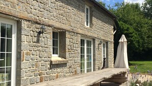 Un bâtiment en pierre doté d’une terrasse en bois et d’un espace extérieur aménagé pour s’asseoir.