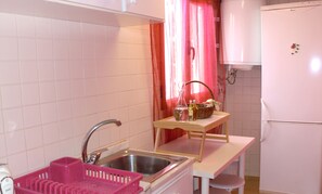 A kitchen with white tiles, a sink, a pink dish rack, a wooden table with a basket, and a white refrigerator. - The Yellow House :) (Vila Nova de Gaia)