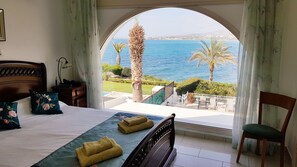 A bedroom with a view of the sea, a bed with towels, a wooden headboard, and a chair.